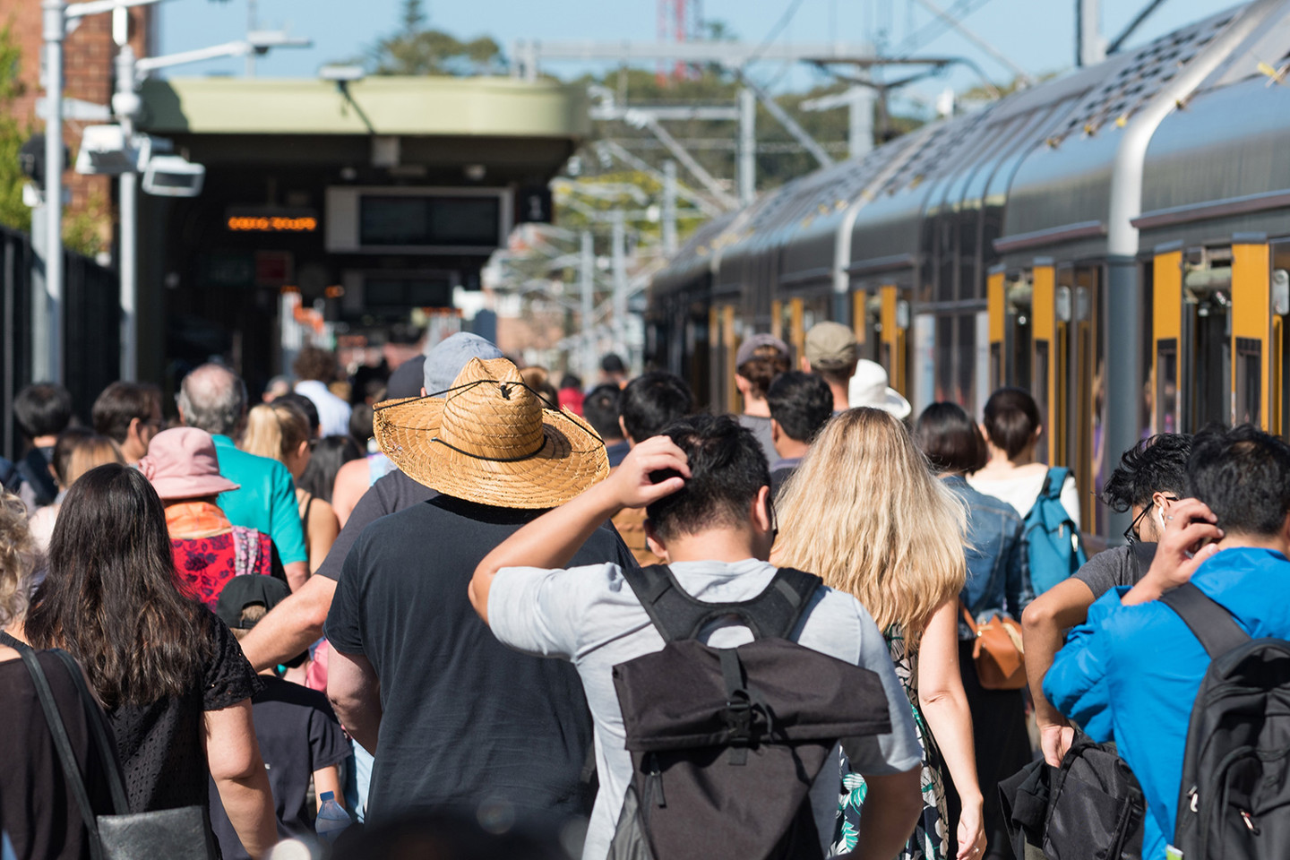 Crowd congregates on train station platform with a gaggle of people all walking in the same direction on the platform with the train to the side. 