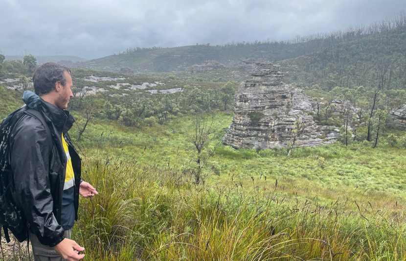 RPS environmental scientist Tam Durney wears protective rain gear as he makes his way through scrubland. 