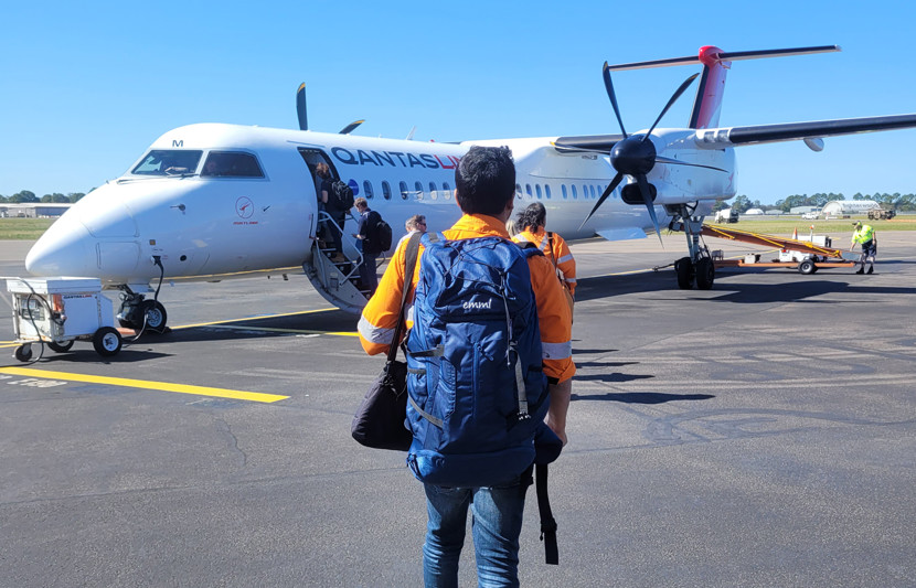 RPS environmental scientists wear orange high-vis and blue backpacks and walk across a tarmac towards a light aircraft. 