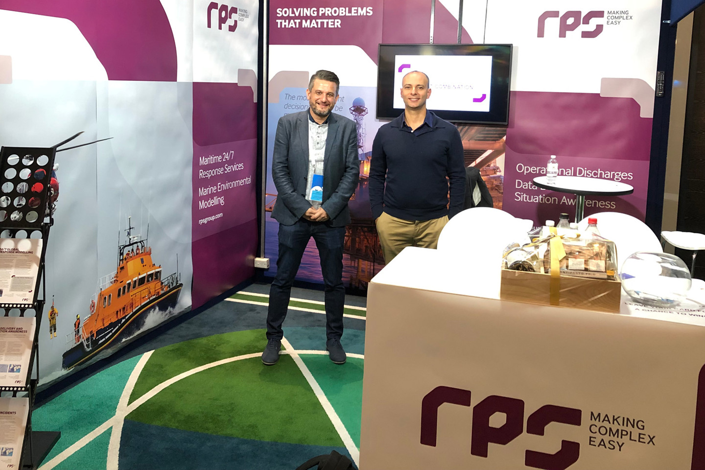 Dr. Sasha Zigic RPS' General Manager - Ocean Science and Technology at a trade show surrounded by RPS branded booths  